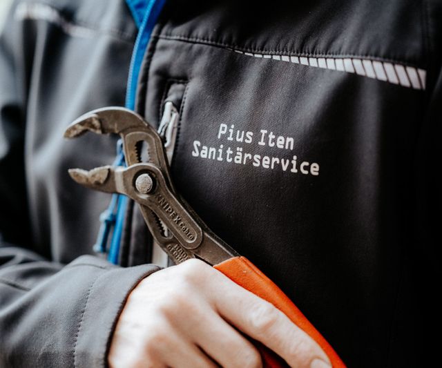 Rohrzange und Arbeitsjacke mit dem Schriftzug Pius Iten Sanitärservice